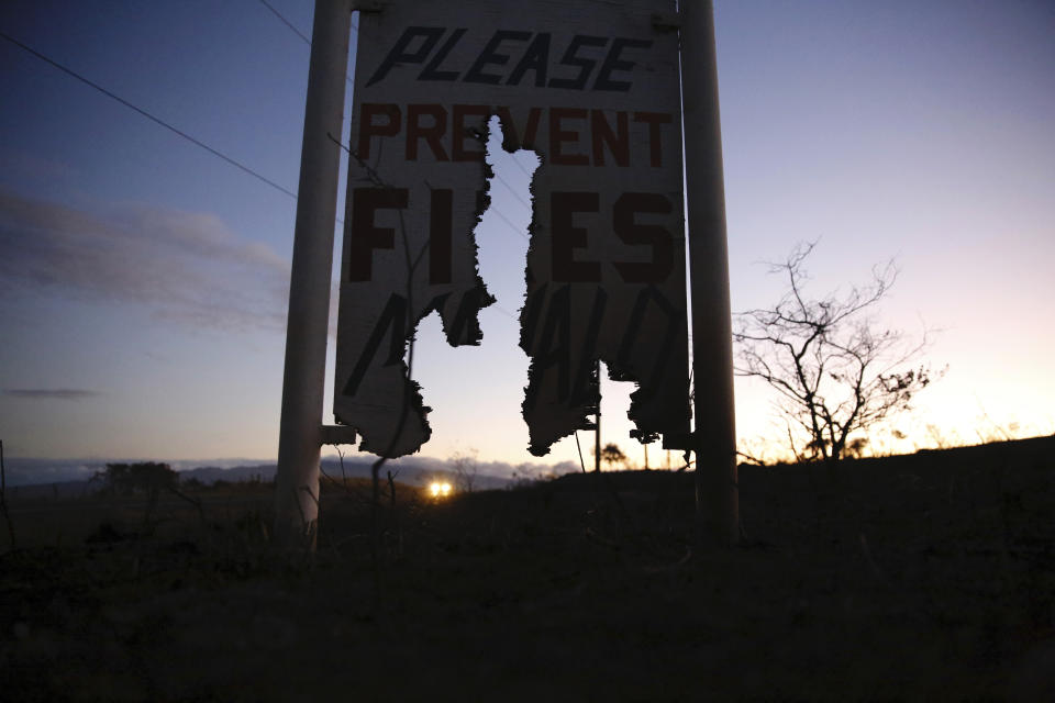 A car drives by a burnt roadside sign that says, "Please Prevent Fires, Mahalo," on Thursday, Aug. 5, 2021, in Waimea, Hawaii. The region was scorched by the state's largest-ever wildfire. (AP Photo/Caleb Jones)