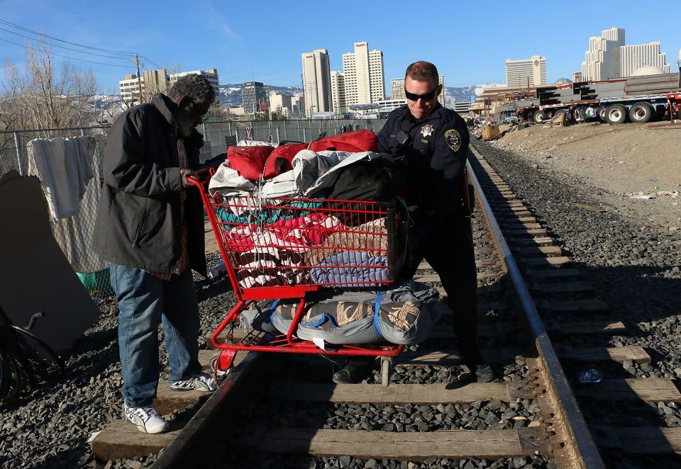 A Reno Police Department officer helps Stephen Frazier get over the tracks with his belongings while being evicted from a homeless encampment in Reno, Nev., on Wednesday.