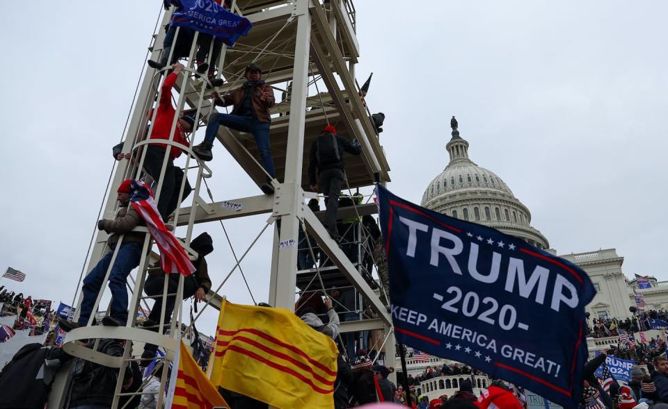 Rioters scale structures while flying flags outside the Capitol.