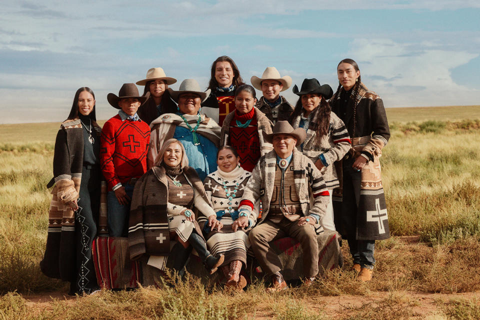 A dozen Native people who worked on the Polo Ralph Lauren x Naiomi Glasses campaign pose in a field for a group photo.