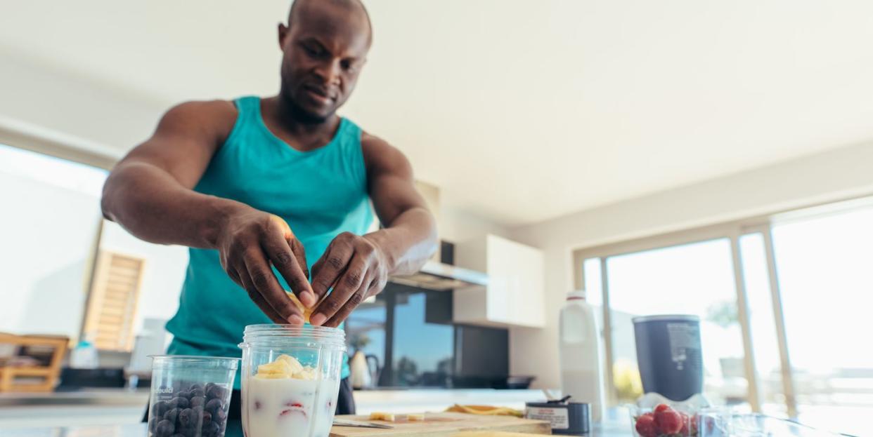 man preparing milk shake in kitchen athletic man adding fruits to jar of milk