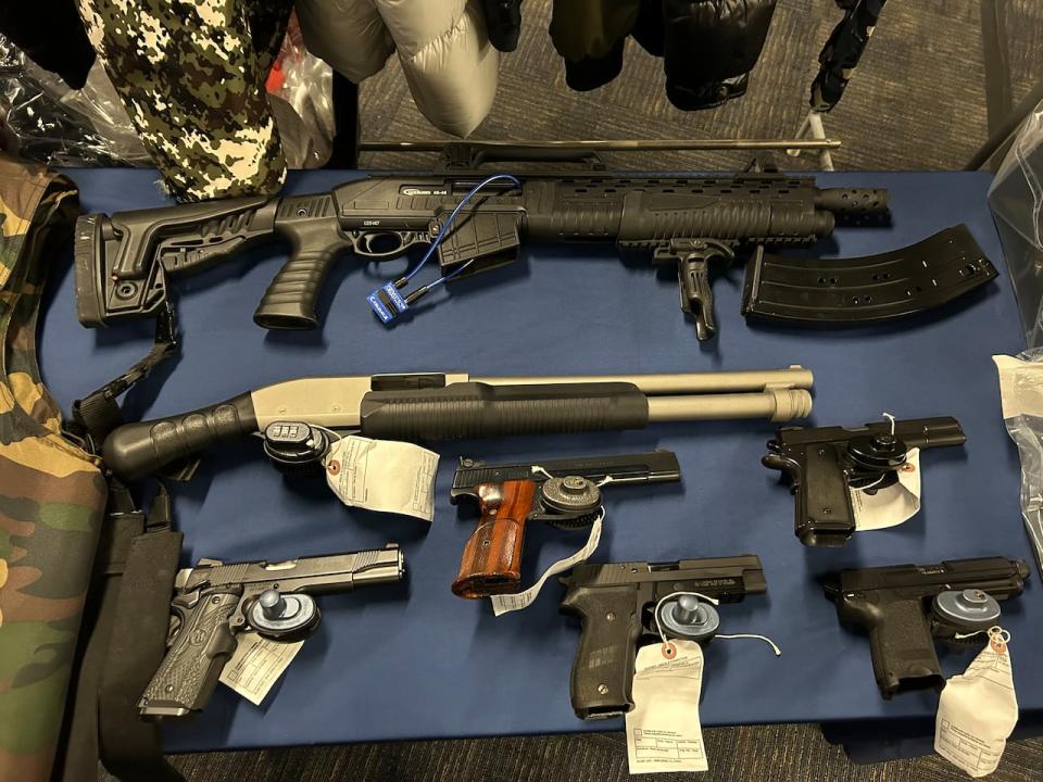A series of guns are laid out on a table next to a bullet proof vest and items seized as part of Manitoba RCMP's Project Decrypt investigation during a news conference in Winnipeg on Tuesday, Dec. 5, 2023. 