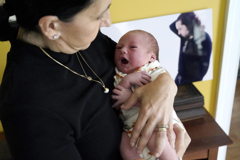 Mercedes Lemp poses for The Associated Press by holding her 2-day-old grandson near a portrait of the newborn's father and their son Duncan Lemp, Friday, Oct. 16, 2020, in Frederick, Md. The Lemps are dealing with the death of their son, who was shot at their home in Potomac, Md., during a no-knock police raid on March 12. Lemp's family have said through their attorney that, based on an eyewitness, they believe Lemp was shot without warning while he was asleep. (AP Photo/Julio Cortez)