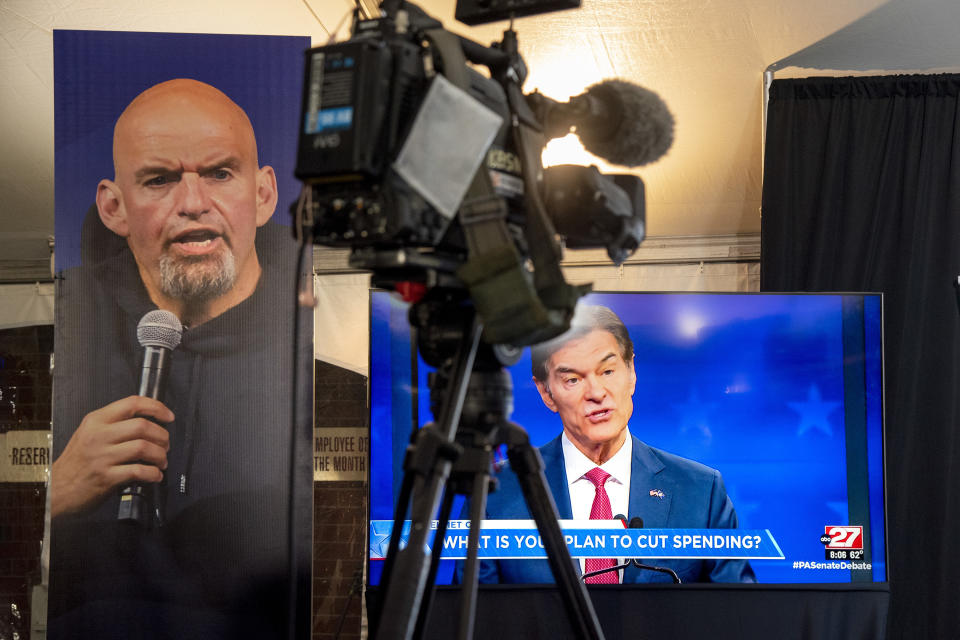 FILE - Republican Mehmet Oz, right, is seen live on a monitor in the media tent, next to a poster of Democrat John Fetterman, left, as the two U.S. Senate candidates hold their first and only debate, at the WHTM-TV/ABC 27 Studio in Harrisburg, Pa., Oct. 25, 2022. With inflation a top concern for voters, many Republican candidates are seeking to capitalize on Americans’ precarious financial situations heading into next week’s midterm elections to vilify a key component of President Joe Biden’s climate agenda: electric vehicles. (Tom Gralish/The Philadelphia Inquirer via AP, File)