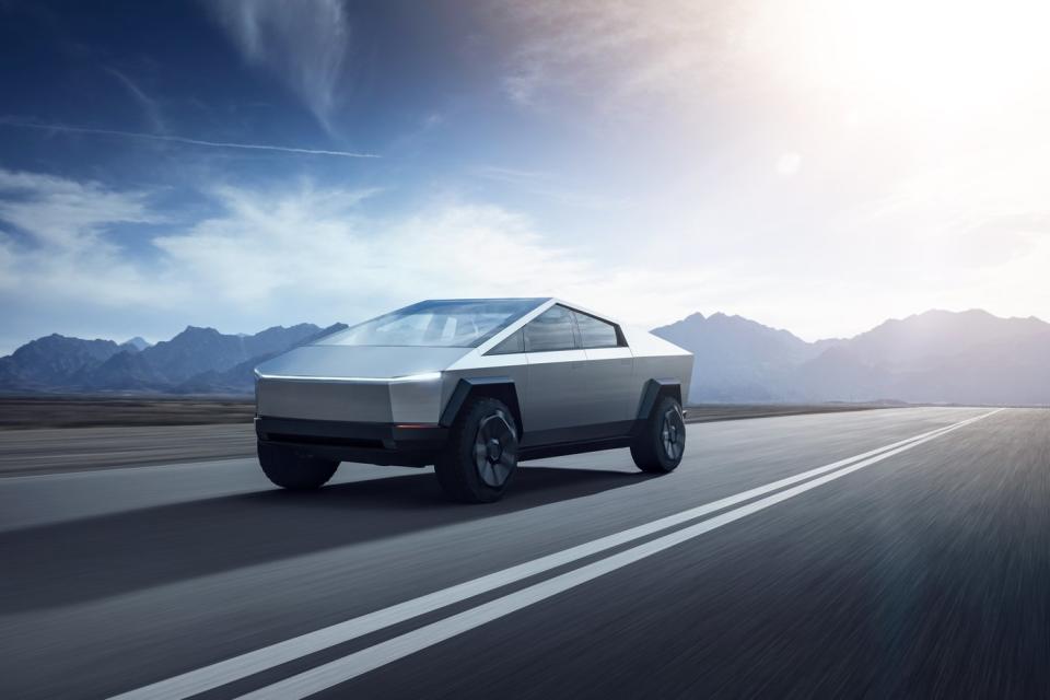 An all-electric Tesla Cybertruck driving on a one-lane road, with mountains in the background.