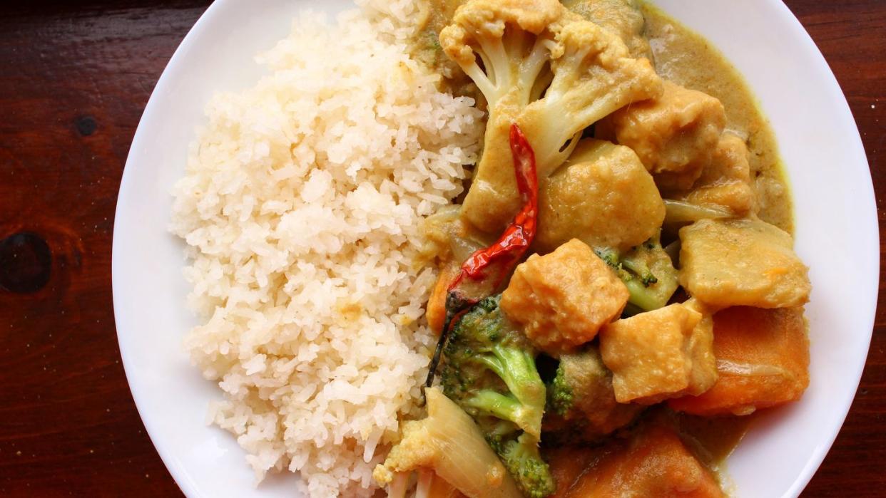 a shallow bowl of sticky white rice and sweet potato curry with cauliflower and broccoli and tofu puffs