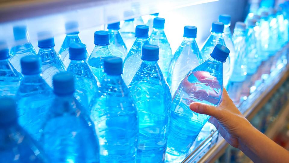 Female hand taking bottle of water from shelf.