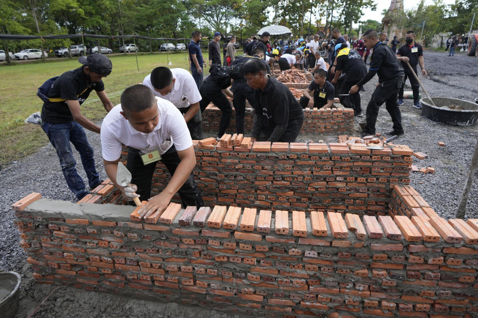 A police officer helps lay bricks for cremation furnaces at Wat Rat Samakee temple in Uthai Sawan, northeastern Thailand, Monday, Oct. 10, 2022. The furnaces were being built Monday to cremate the bodies of the mostly young victims of last week’s massacre at a day care center by a former policeman. (AP Photo/Sakchai Lalit)