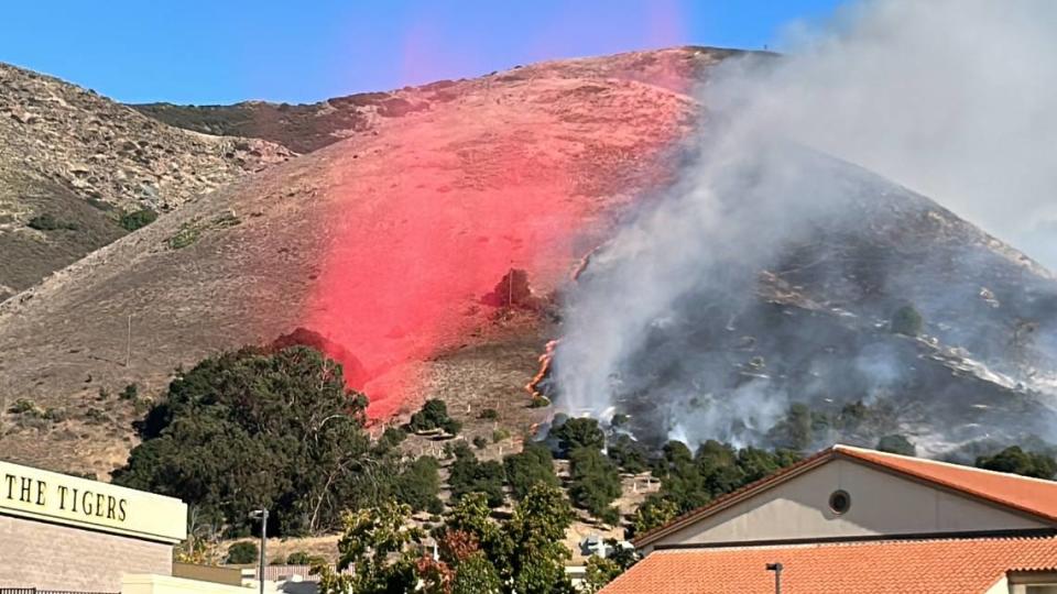 A cloud of retardant falls onto a line of flames as a fire burns behind San Luis Obispo High School on Monday, Oct. 30, 2023.