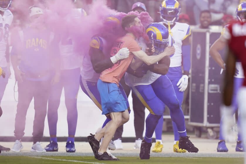 A protester carrying a smoke bomb is hit by Rams defensive end Takkarist McKinley and linebacker Bobby Wagner