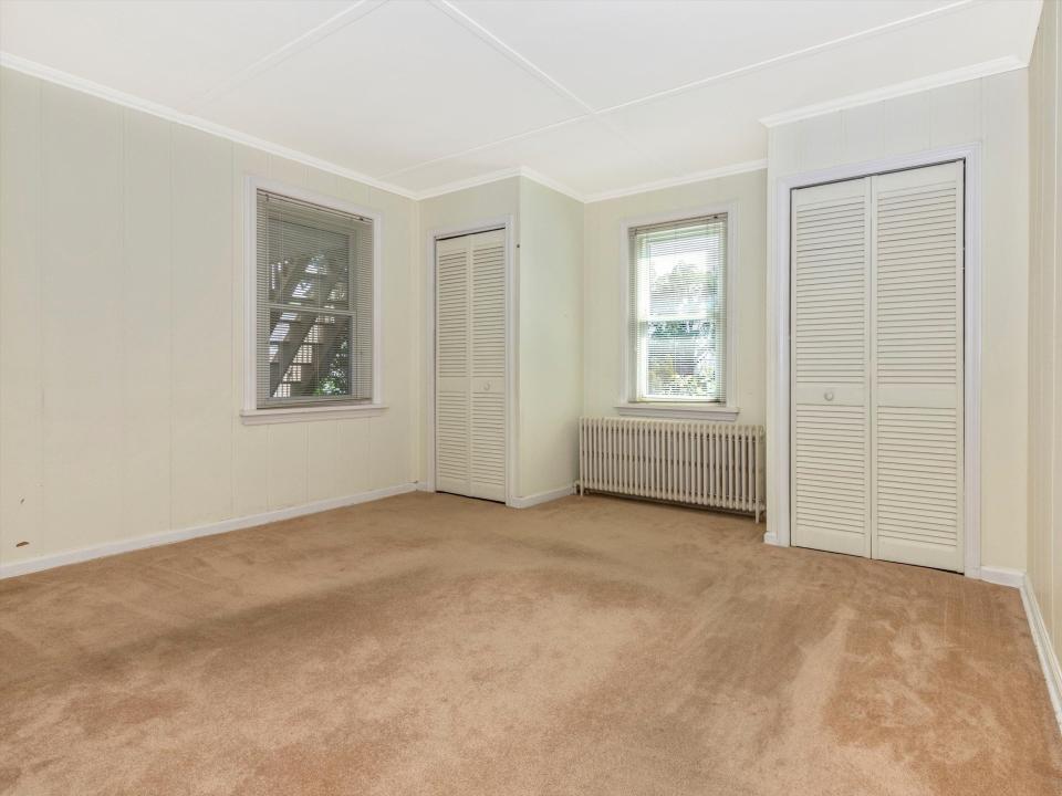 an empty bedroom with a carpet and two windows