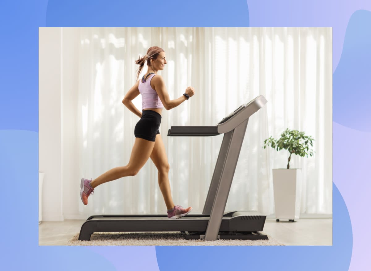 happy blonde woman in pink tank top and black biker shorts running on treadmill at home in bright living space in front of curtain window