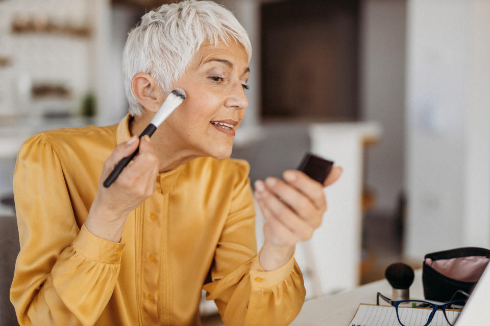 mature woman applying makeup to face