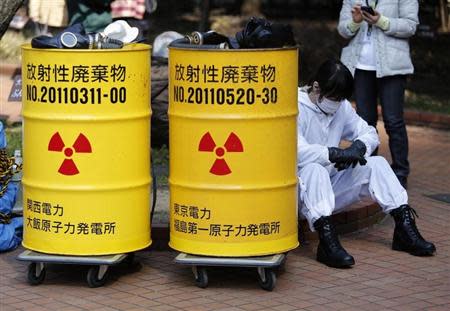 An anti-nuclear protester wearing protective suit sits next to mock drums labelled as radioactive waste from Kansai Electric Power Co's Ohi nuclear power plant (L) and Tokyo Electric Power Co's (TEPCO) Fukushima nuclear power plant, before a march in Tokyo March 9, 2014. REUTERS/Yuya Shino