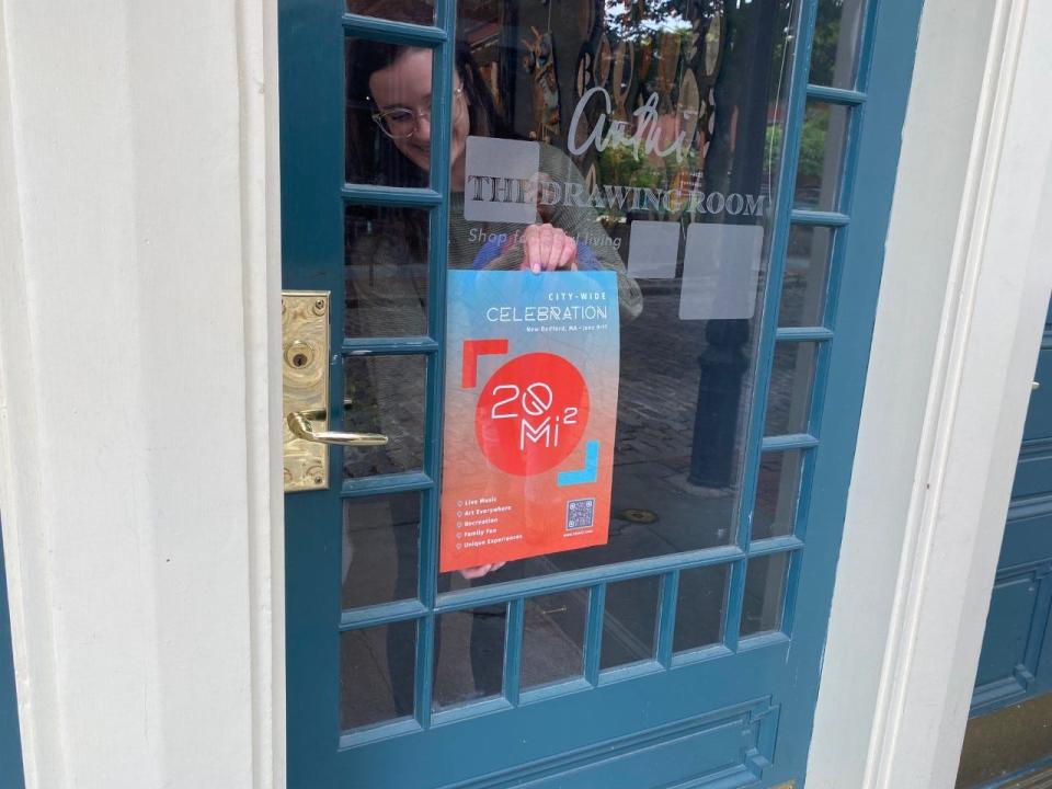 Shayla Manning hangs a poster for the 20mi2 celebration in the window of The Drawing Room in New Bedford.