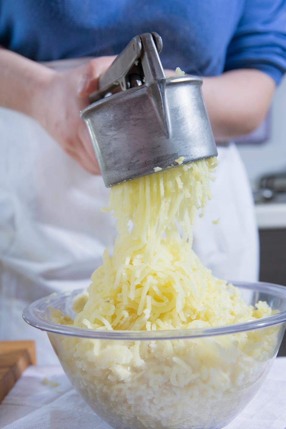 someone pressing potatoes through a potato ricer into a large bowl