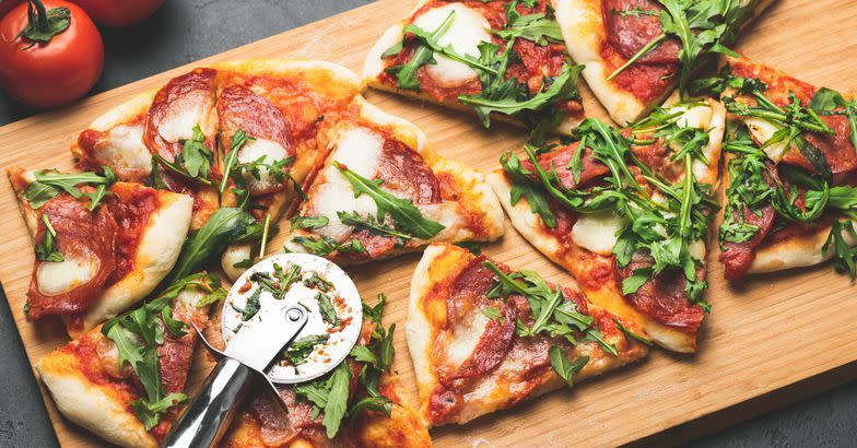 Pizza or flatbread with arugula, salami, cheese sliced ​​on wooden cutting pizza board