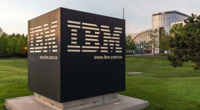 Quantum computing stocks: Sign of IBM with Canada Head Office Building in background in Markham, Ontario, Canada. IBM is an American multinational technology company.