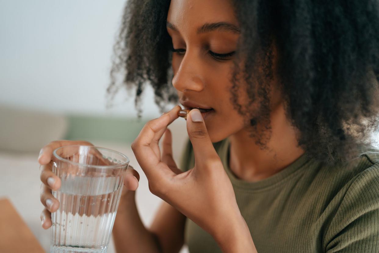 Young African American girl using tablet or medical pill and holding glass of water. Healthy lifestyle, vitamin dieting.