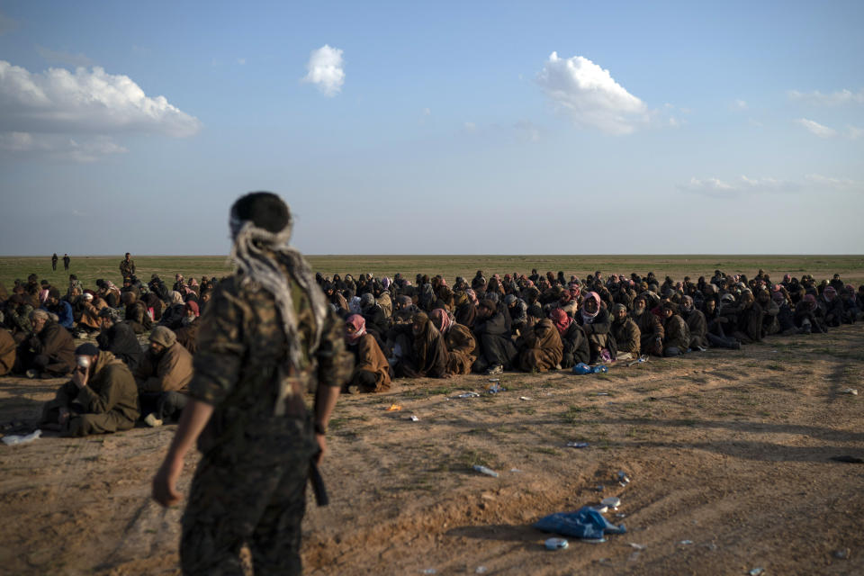 U.S.-backed Syrian Democratic Forces (SDF) fighters stand guard next to men waiting to be screened after being evacuated out of the last territory held by Islamic State militants, near Baghouz, eastern Syria, Friday, Feb. 22, 2019. (AP Photo/Felipe Dana)