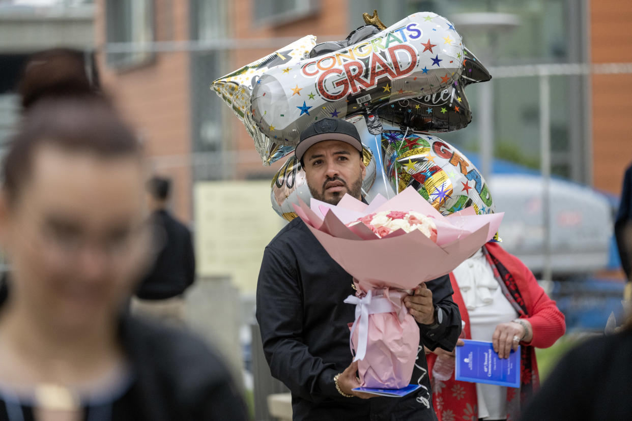 A man carries flowers and balloons to a graduation.