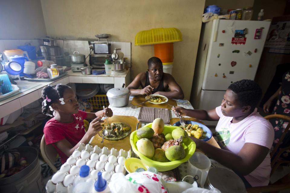 Franchina 11, left, eats lunch with her foster family, Pastor Jeannes Pierre and his daughter Jenny Pierre in their home in Port-au-Prince, Haiti on Saturday, June 30, 2018. The Pierres do not know how long Franchina might stay with them, given uncertainty about her father's status. "We want to keep her as long as possible," Pierre said. (AP Photo/Dieu Nalio Chery)