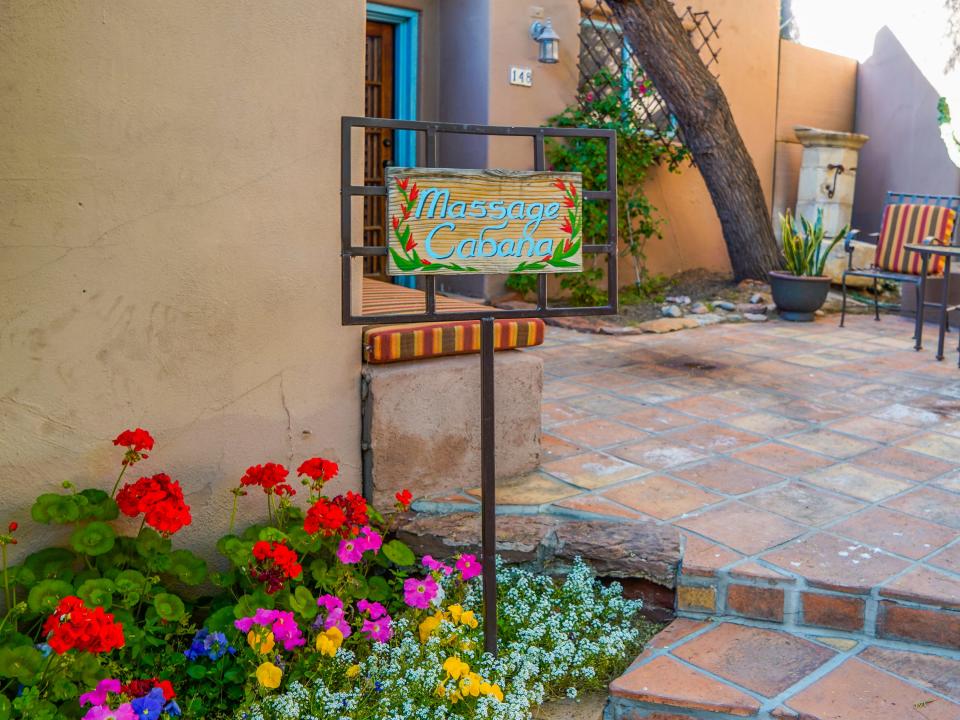 A sign in front of a tan adobe building says "Massage Cabana" over a bed of flowers