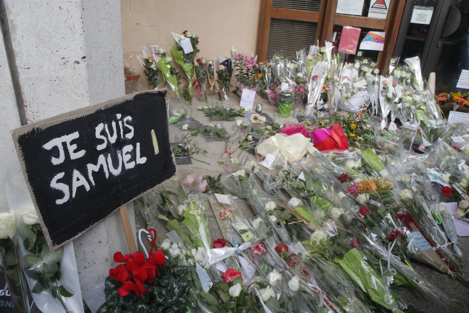 FILE - A poster reading "I am Samuel" and flowers lay outside the school where slain history teacher Samuel Paty was working, Saturday, Oct. 17, 2020 in Conflans-Sainte-Honorine, northwest of Paris. A French juvenile court is handing down a verdict Friday dec.8, 2023 for six teenagers accused of involvement in the killing of teacher Samuel Paty, beheaded by an Islamic extremist after he showed caricatures of the Prophet Muhammad to his class for a debate on freedom of expression. (AP Photo/Michel Euler, File)