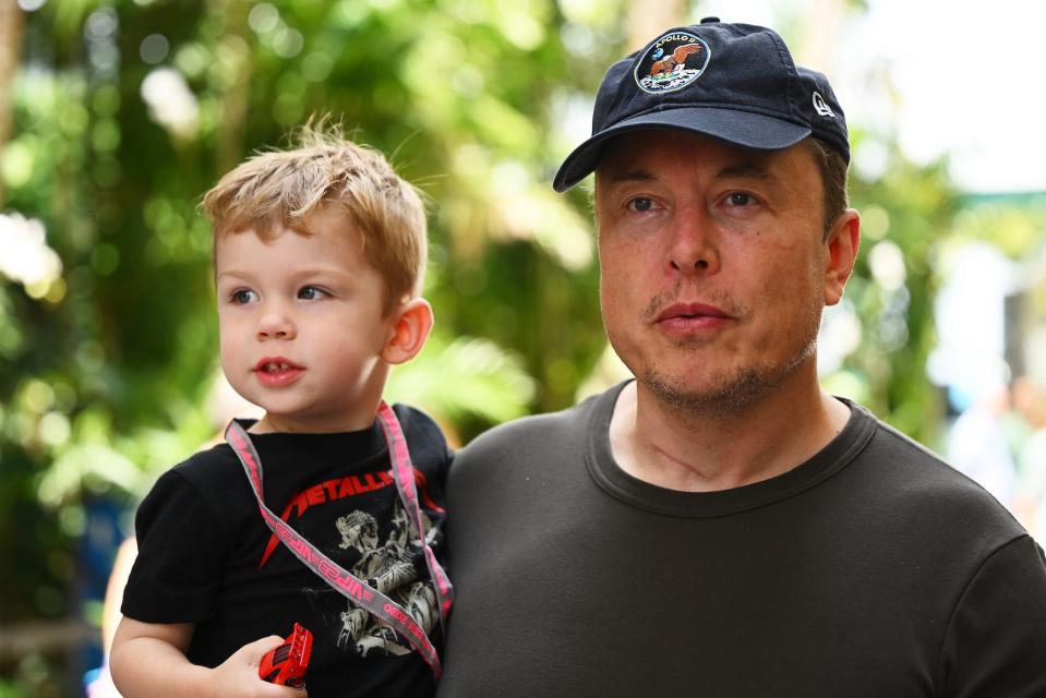 Elon Musk wears a baseball cap and holds his son X, his oldest child with Grimes.