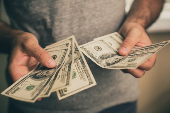 A man holds several hundred dollar bills in his hand.