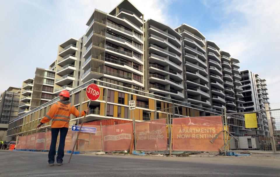 A worker holding a stop sign in front of an apartment block under construction. (Source: Getty)