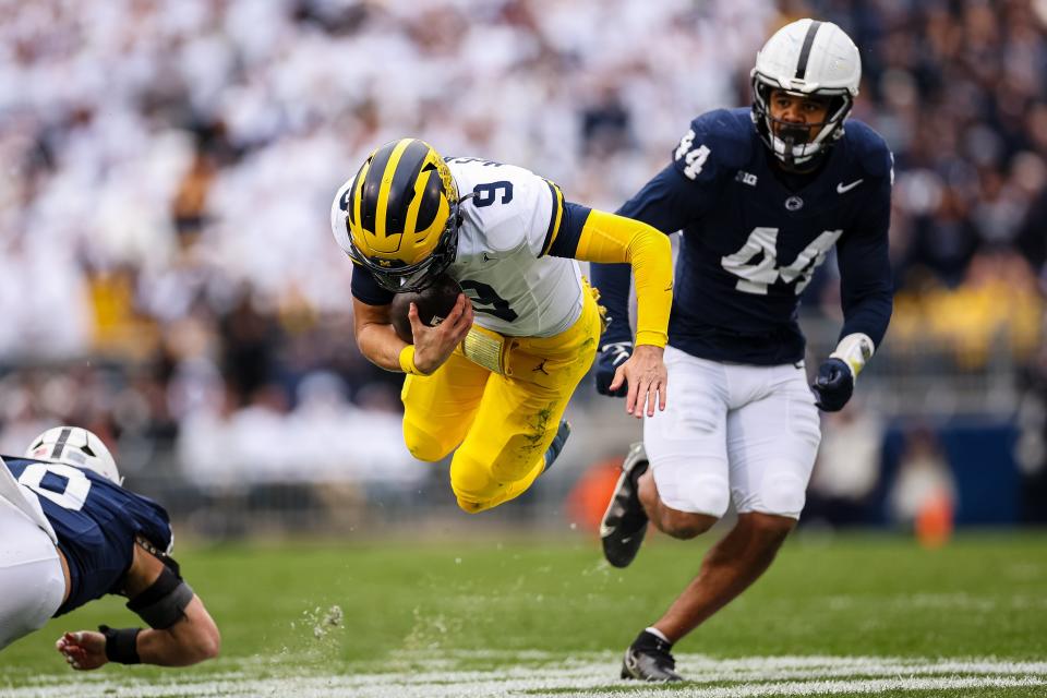 J.J. McCarthy of the Michigan Wolverines goes airborne after being tripped up in front of Chop Robinson of the Penn State Nittany Lions during the second half at Beaver Stadium on November 11, 2023 in State College, Pennsylvania.