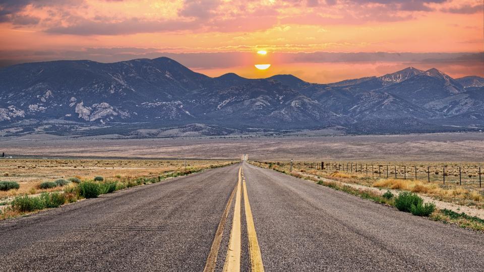 great basin national park road stretching off into the distance with mountains and a setting sun in the background.