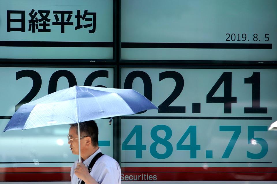 A man with a parasol walks past an electronic stock board showing Japan's Nikkei 225 index at a securities firm in Tokyo Monday, Aug. 5, 2019.