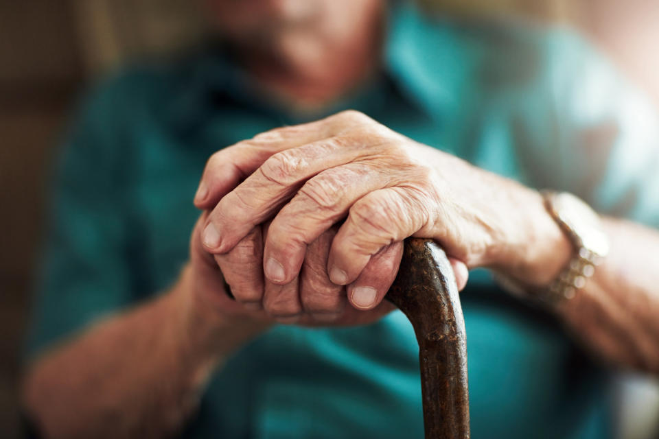 Closeup of an old man's hands resting on his cane