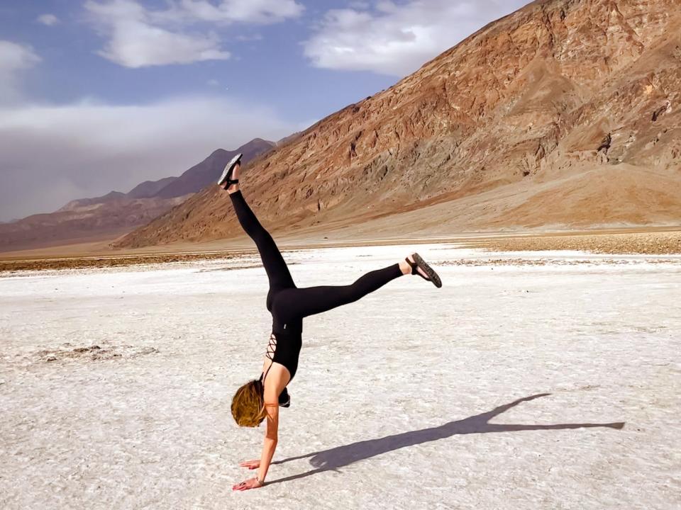 Emily does a handstand on the sand in Death Valley National Park. There are mountains behind her.