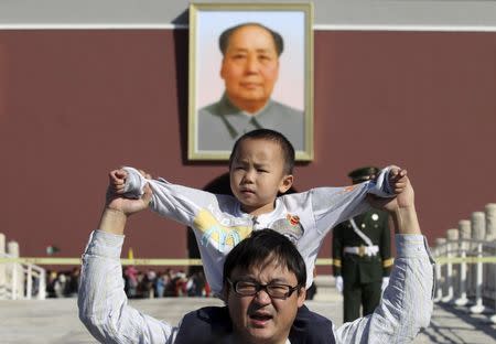 A boy sits on his father's shoulders as they pose for a photograph in front of the giant portrait of late Chinese chairman Mao Zedong on the Tiananmen Gate, in Beijing, China, October 2, 2011. REUTERS/Stringer