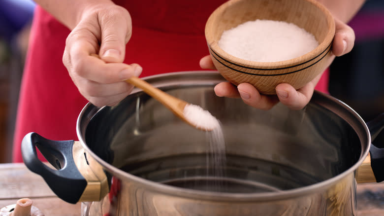 hands spooning salt into water