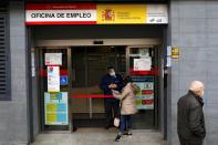 An employee wearing a protective shield talks to a job seeker outside a government job center during the coronavirus disease (COVID-19) outbreak in Madrid