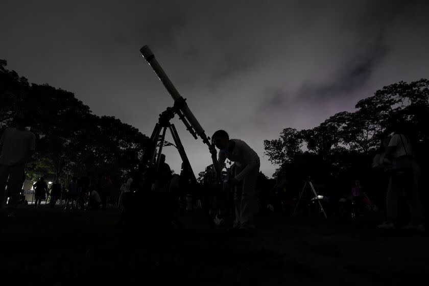 FILE - A girl looks at the moon through a telescope in Caracas, Venezuela, on Sunday, May 15, 2022. The best day to spot five planets, Mercury, Jupiter, Venus, Uranus and Mars, lined up in the night sky is Tuesday, March 28, 2023, right after sunset. The five-planet array will be visible from anywhere on Earth, as long as you have clear skies. (AP Photo/Matias Delacroix)