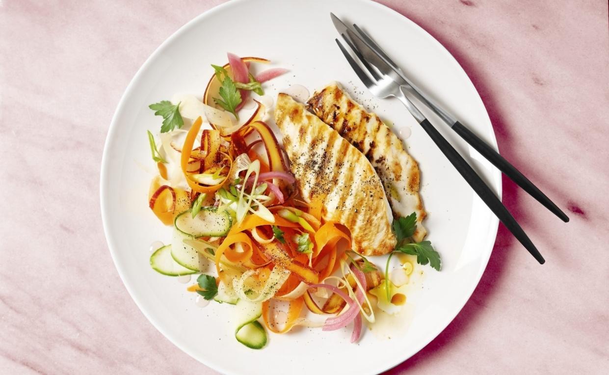 A plate of grilled chicken with carrot salad on white background