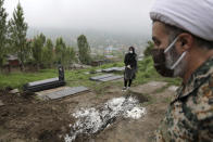 FILE - In this April 30, 2020, file photo, a woman wearing mask and gloves, prays at the grave of her mother who died from the coronavirus, at a cemetery in the outskirts of the city of Babol, in northern Iran. As coronavirus infections reached new heights in Iran, overwhelming its hospitals and driving up its death toll, the country’s health minister gave a rare speech criticizing his own government’s refusal to enforce basic health measures. (AP Photo/Ebrahim Noroozi, File)