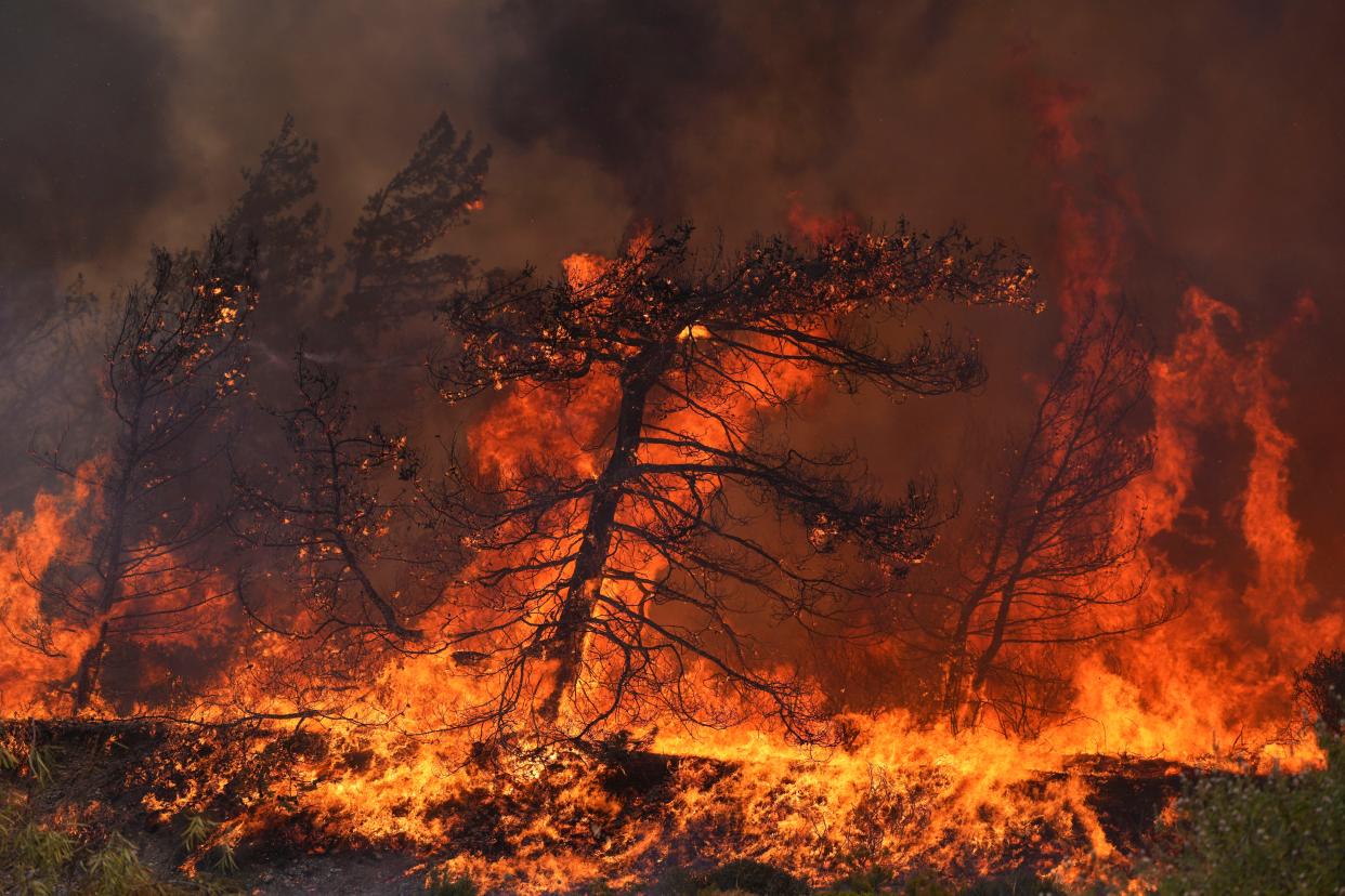 Flames burn a forest in Vati village, on the Aegean Sea island of Rhodes, Greece, on Tuesday. A third successive heat wave in Greece pushed temperatures back above 40 degrees Celsius (104 degrees Fahrenheit) across parts of the country Tuesday following more nighttime evacuations from fires that have raged out of control for days.