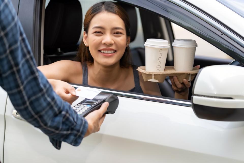 Woman getting 2 drinks from car at a drive-thru.