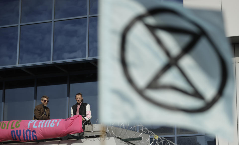 An Extinction Rebellion flag flies as demonstrators occupy a raised area at City Airport in London, Thursday, Oct. 10, 2019. Some hundreds of climate change activists are in London during a fourth day of world protests by the Extinction Rebellion movement to demand more urgent actions to counter global warming. (AP Photo/Matt Dunham)