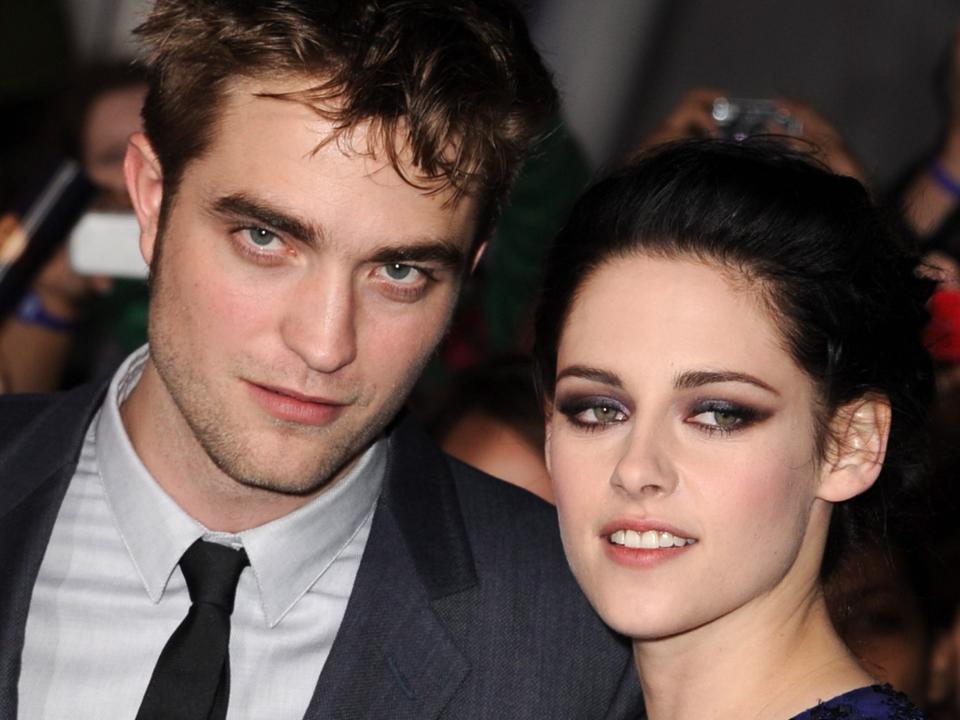 Robert Pattinson, in a gray suit, poses with Kristen Stewart, in a blue dress with rhinestones, on the red carpet at the "Breaking Dawn Part 1" premiere in 2011.