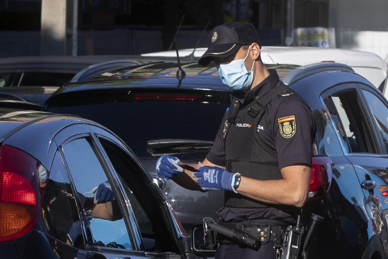 A police officer checks a driver's documents at a checkpoint on the outskirts of Madrid, Spain on Saturday, Oct. 3, 2020. Madrid is on a partial lockdown complying with an order from the Spanish government due to the high COVID-19 cases but determined to fight it in the courts. Measures ban all nonessential trips in and out of the capital and nine of its suburbs, covering around 4.8 million people.