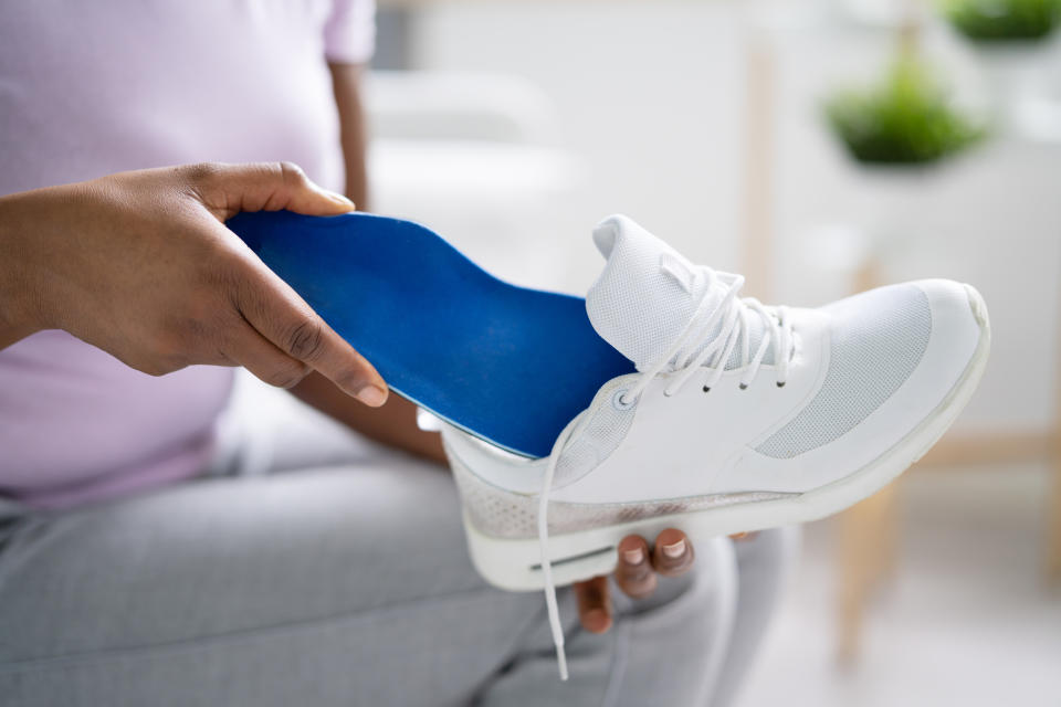 Person inserting an orthotic insole into a white sneaker