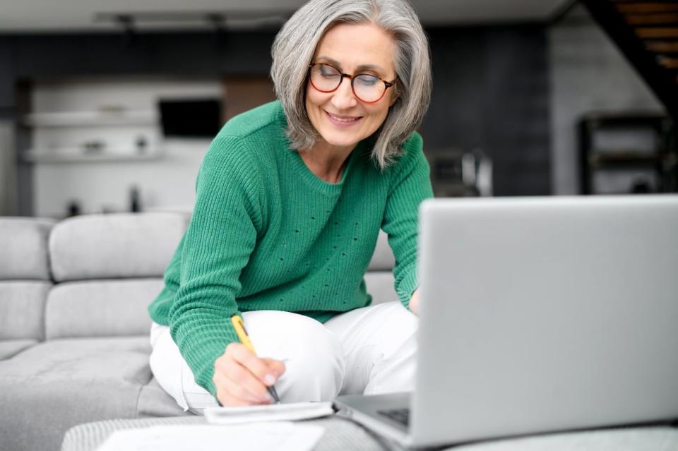 A person writes on a notepad while sitting in front of a laptop. 