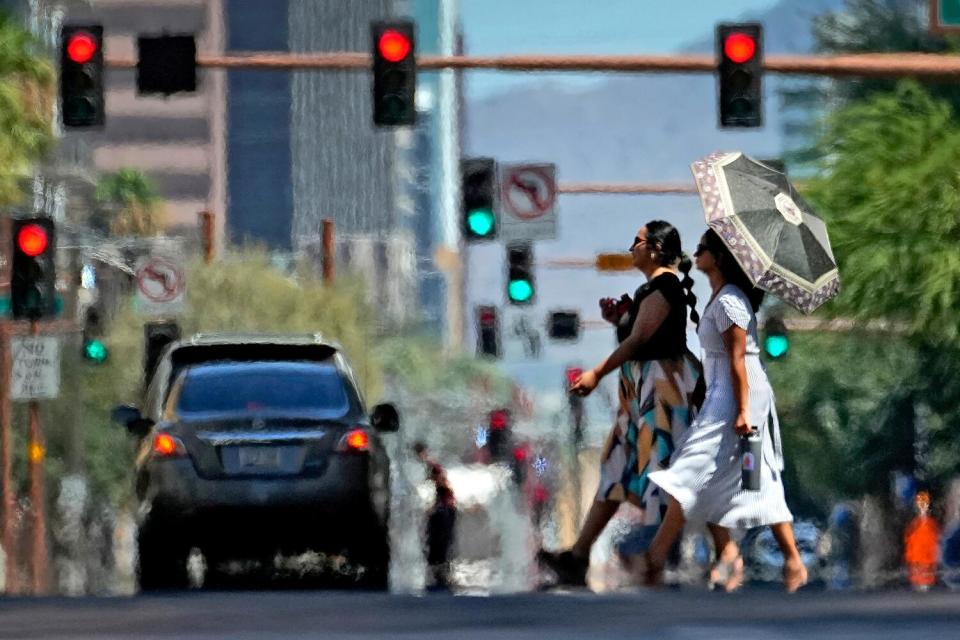 The heat ripples from the hot asphalt as two women cross a street.